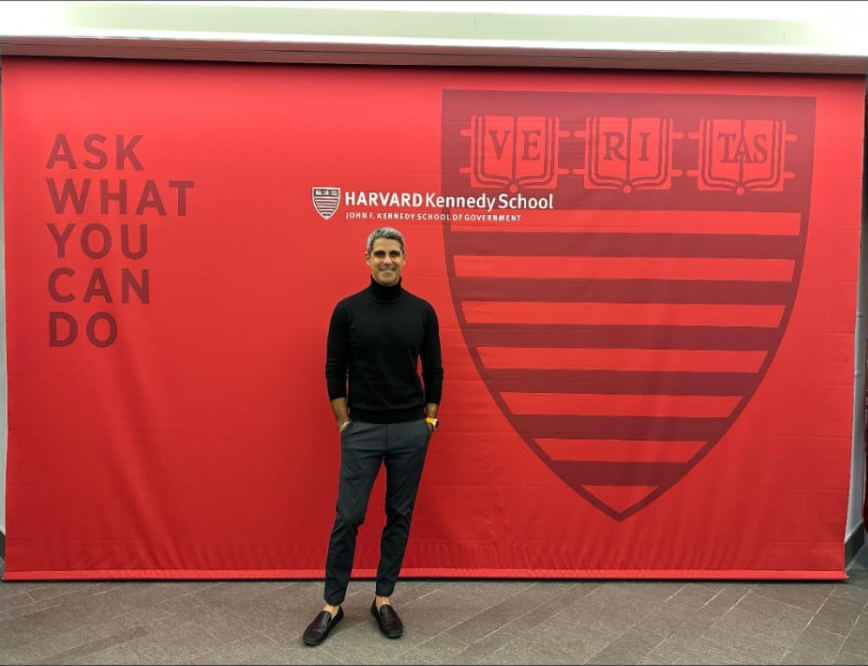 Hamada Zahawi, HKS MPA alumnus, in front of the Harvard Kennedy School banner
